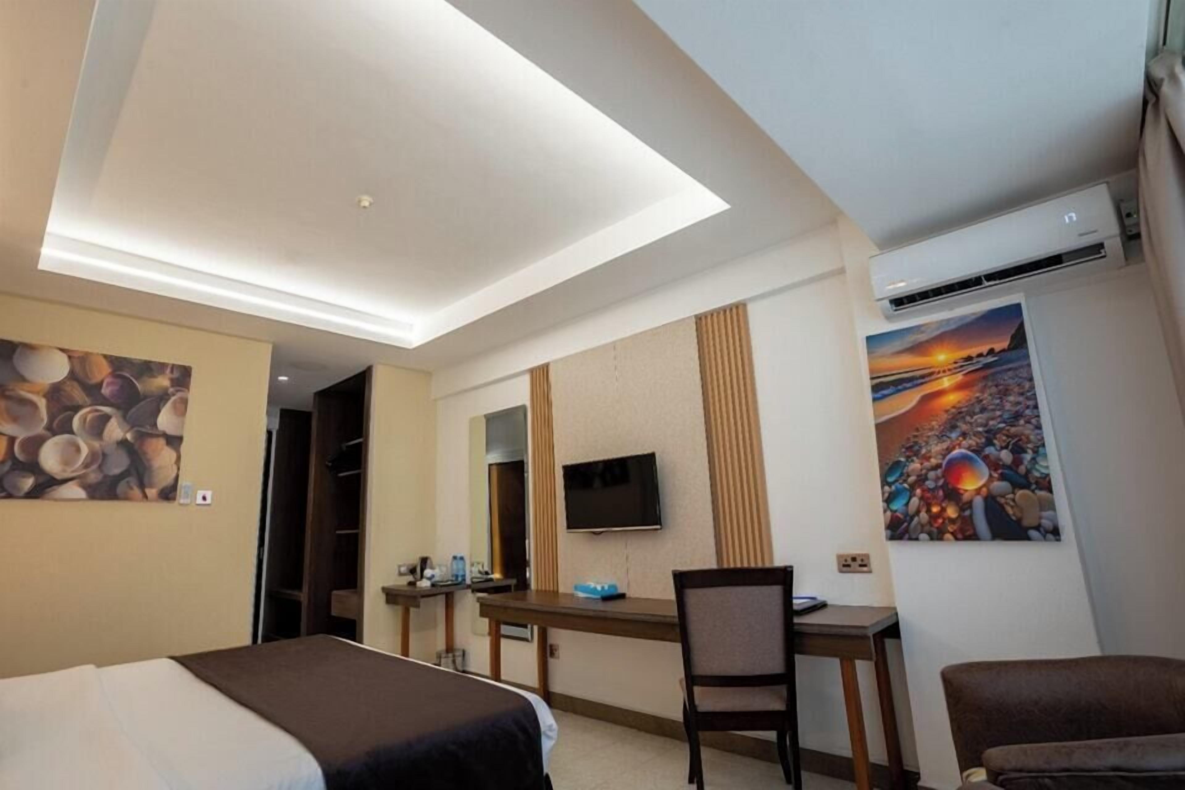 A hotel room with a bed, desk, chair, TV, and artwork on the walls.