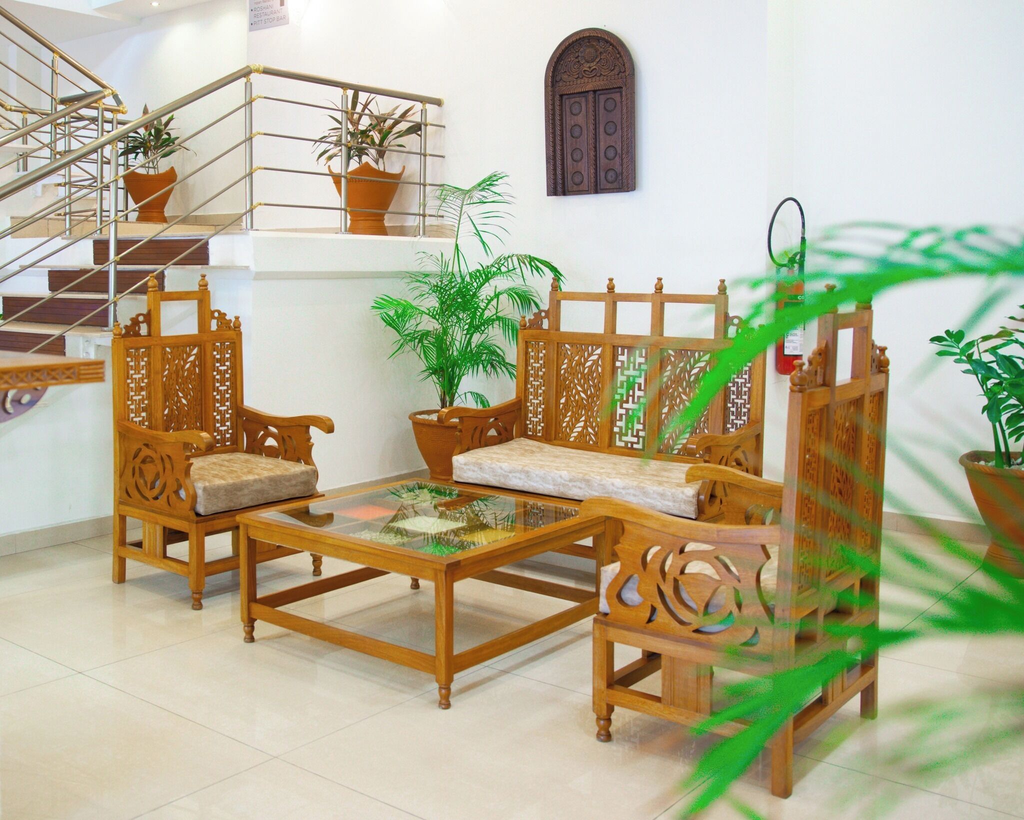 A traditional wooden sofa set with cushions, a glass coffee table, and potted plants.