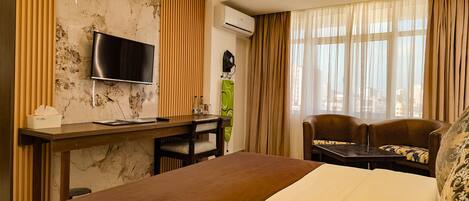 A hotel room with a bed, a desk with a chair, a television, and a window with curtains.