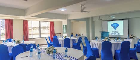 A conference room with round tables, blue chairs, and a projector screen displaying 'HOTEL SAPPHIRE'.