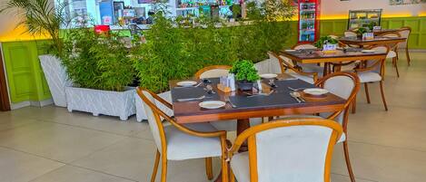 A restaurant with tables set for dining, a bar area in the background, and indoor plants.