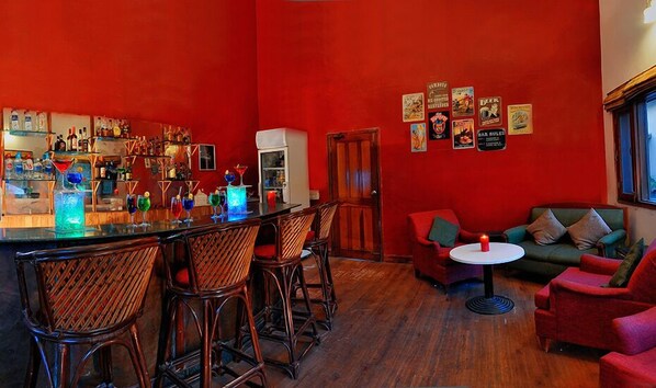 A bar area with stools, a counter, and a seating area with a sofa and chairs. - The Kikar Lodge (Anandpur Sahib)