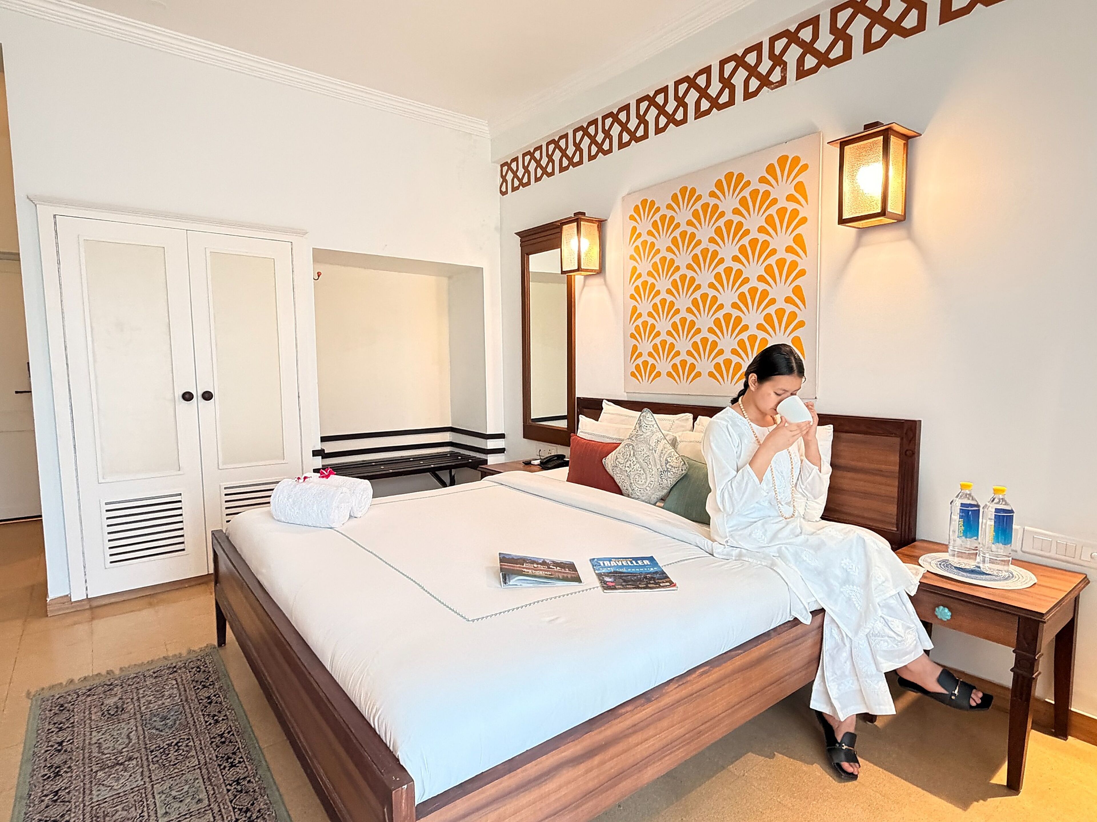 A hotel room with a bed, bedside table, lamp, and a patterned wall decoration.
