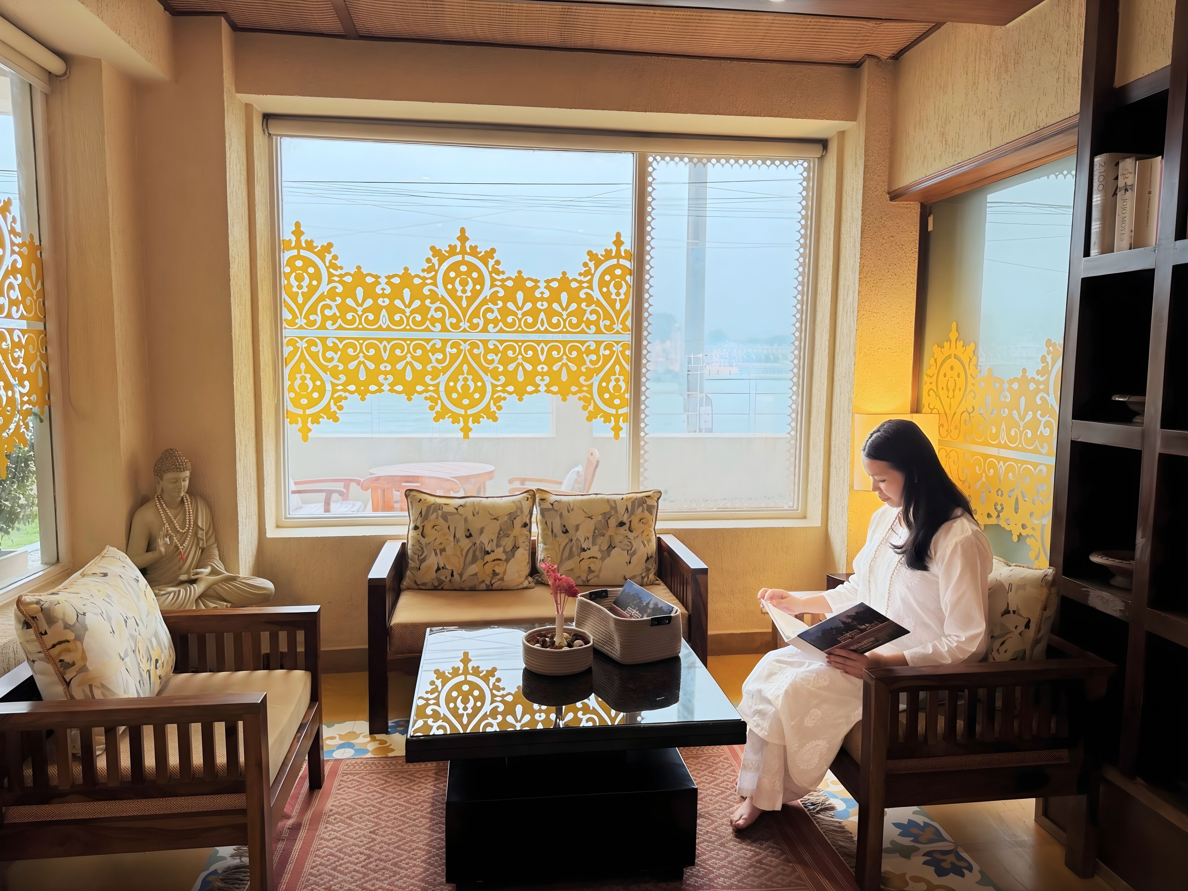 A room with a Buddha statue, a sofa, a table with a decorative tray, and a bookshelf.