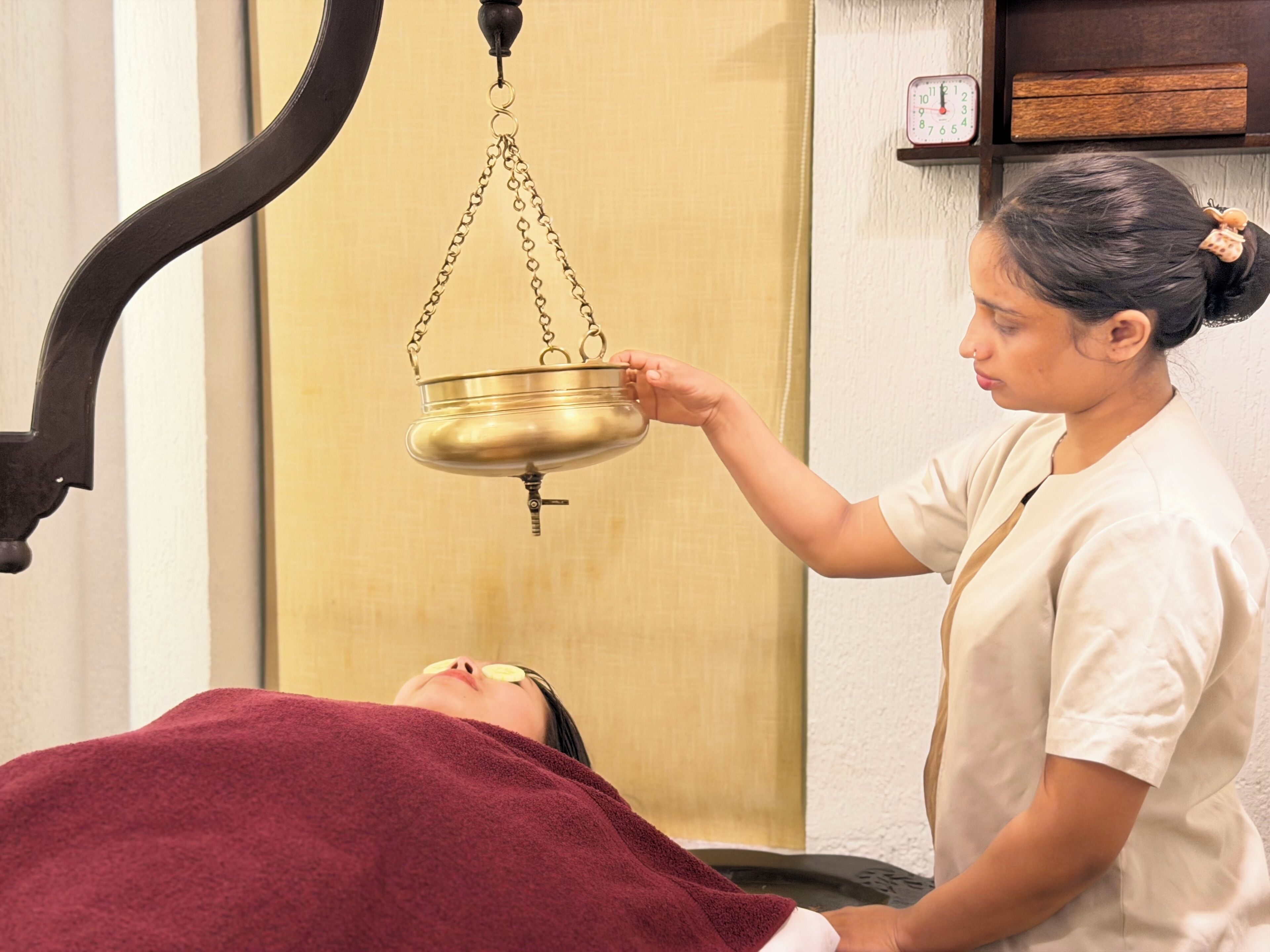 A person receiving a treatment with a metal bowl suspended from the ceiling.