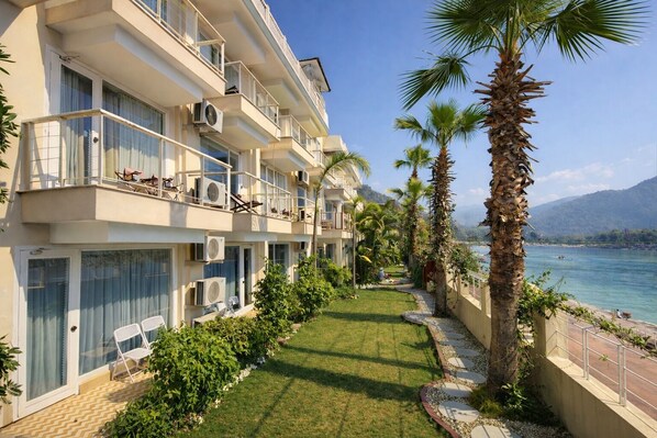 Un hotel de varios pisos con balcones, unidades de aire acondicionado y vista a una masa de agua con palmeras.