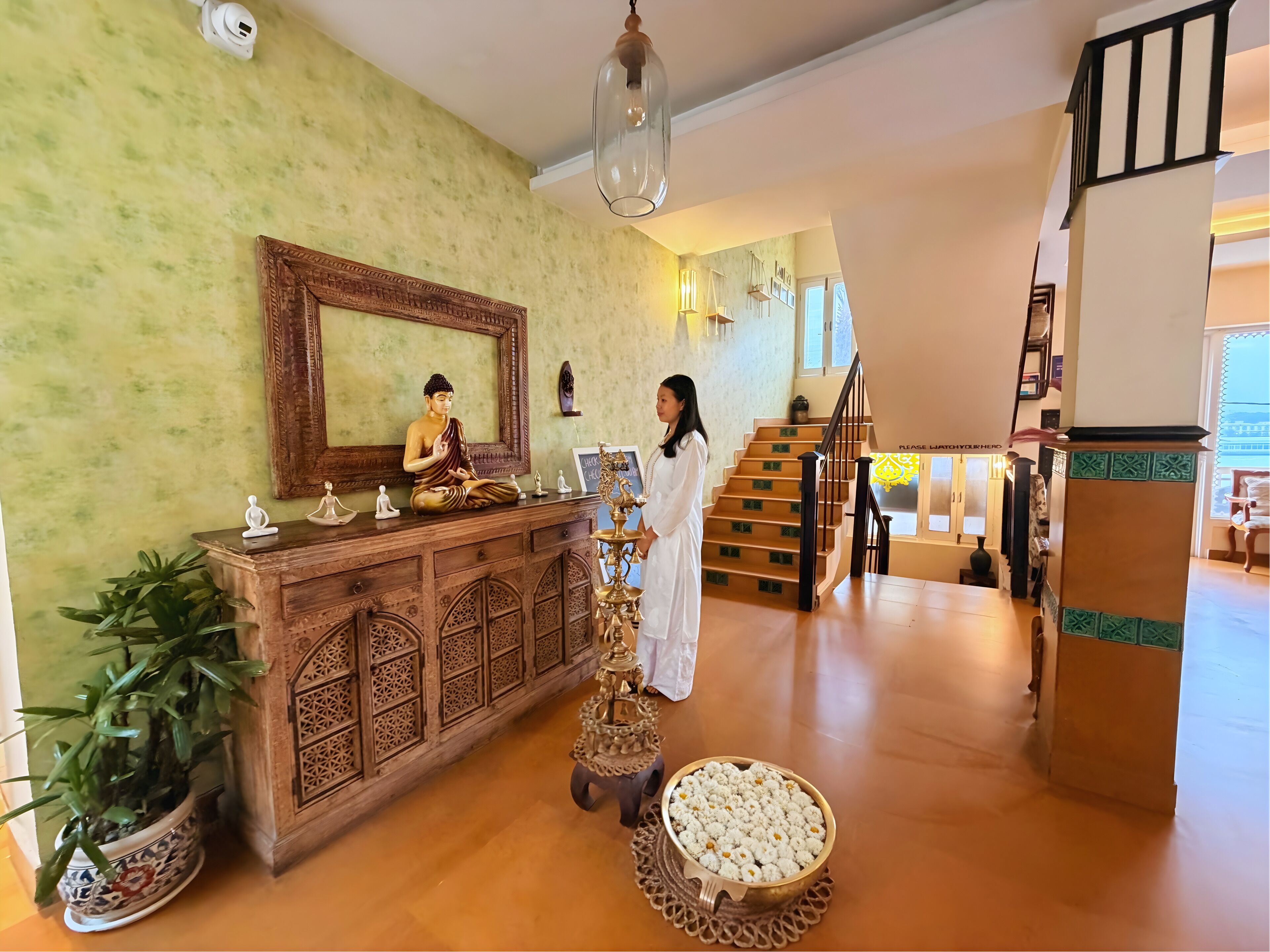 Una habitación con un armario de madera, una estatua de Buda, una planta en maceta, un cuenco decorativo y una escalera.