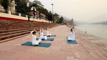 A group of people performing yoga on mats along a riverside walkway.