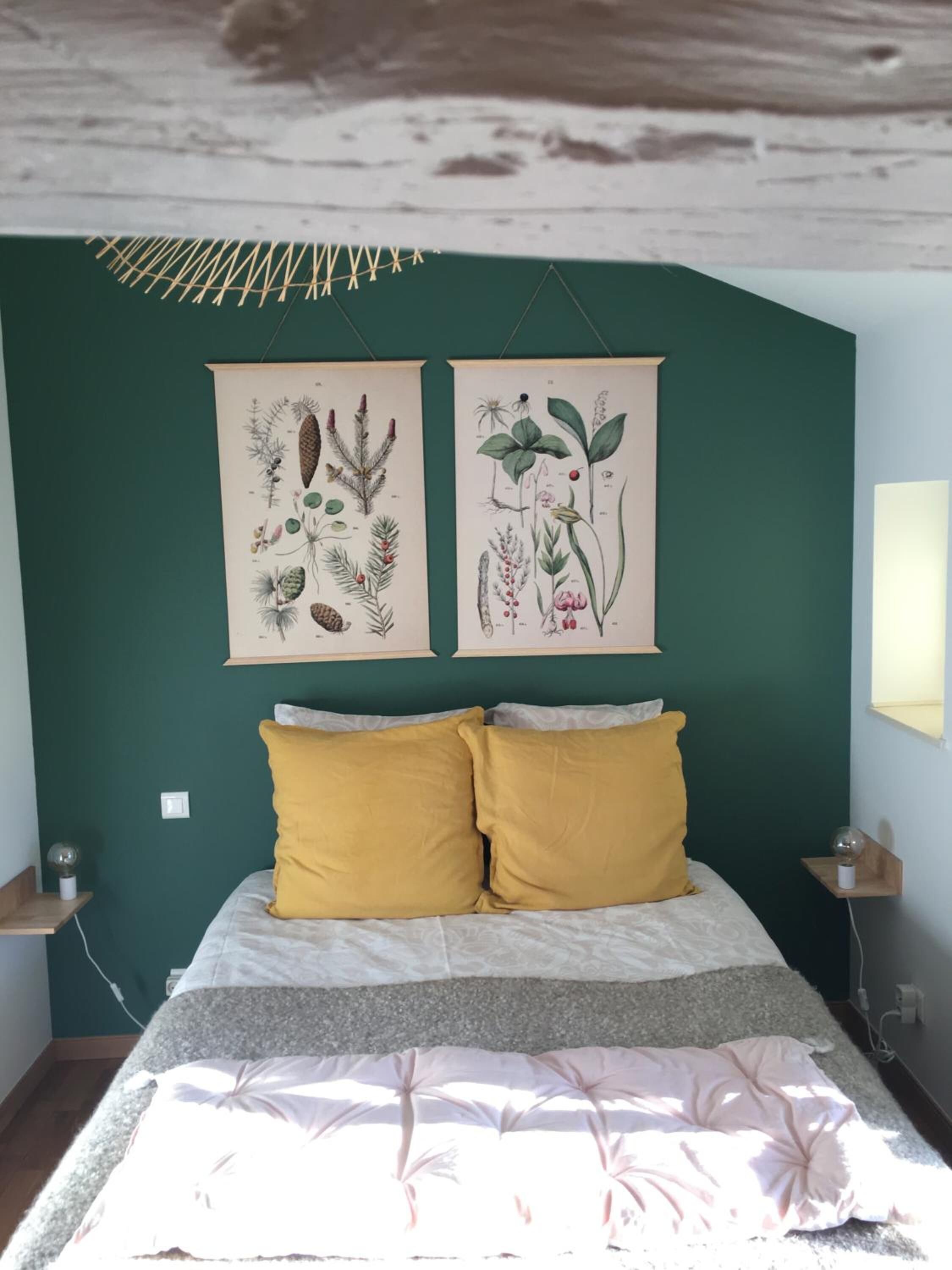 Une chambre à coucher avec un lit, deux oreillers jaunes et deux œuvres d’art murales sur le thème de la botanique.