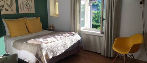 Een slaapkamer met een bed, een raam met gordijnen, een stoel en decoratieve wandkunst.