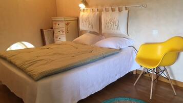 Een slaapkamer met een bed, een gele stoel, een nachtkastje en een wandlamp.
