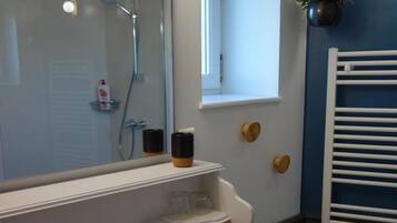 A bathroom with a white sink, mirror, and vanity, a shower with a glass door, and a potted plant on the wall.