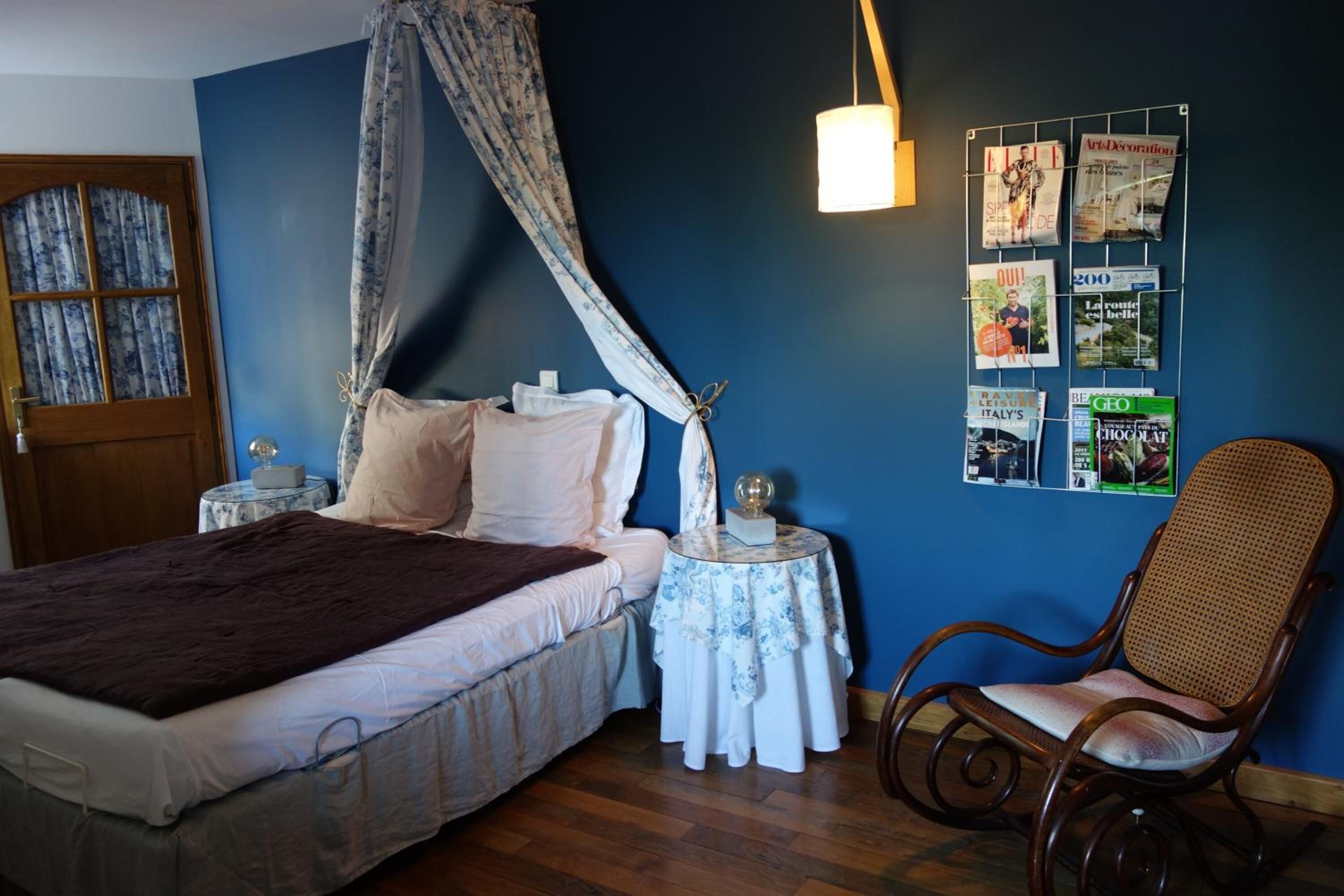 A bedroom with a bed, a chair, a bedside table, and a wall with magazines.