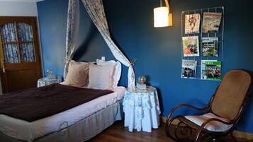 A bedroom with a bed, a chair, a bedside table, and a wall with magazines.