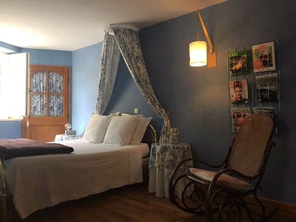 A bedroom with a bed, a chair, a table with a lamp, and a wall with magazines. - Chambres d'hôtes Les Picorettes  (Vaux-en-Beaujolais)