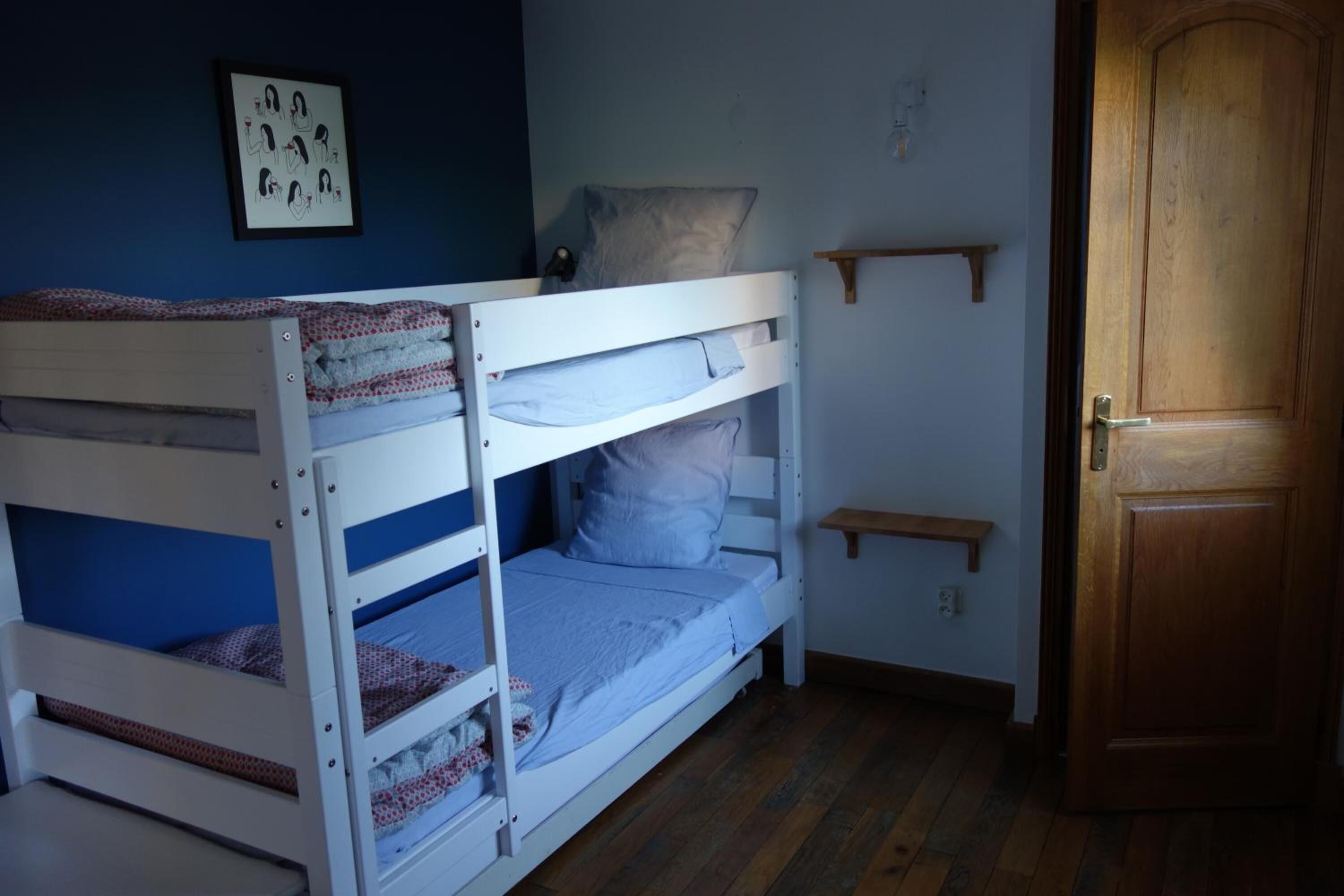 A bunk bed room with a wooden door, a small shelf, and a framed picture on the wall.