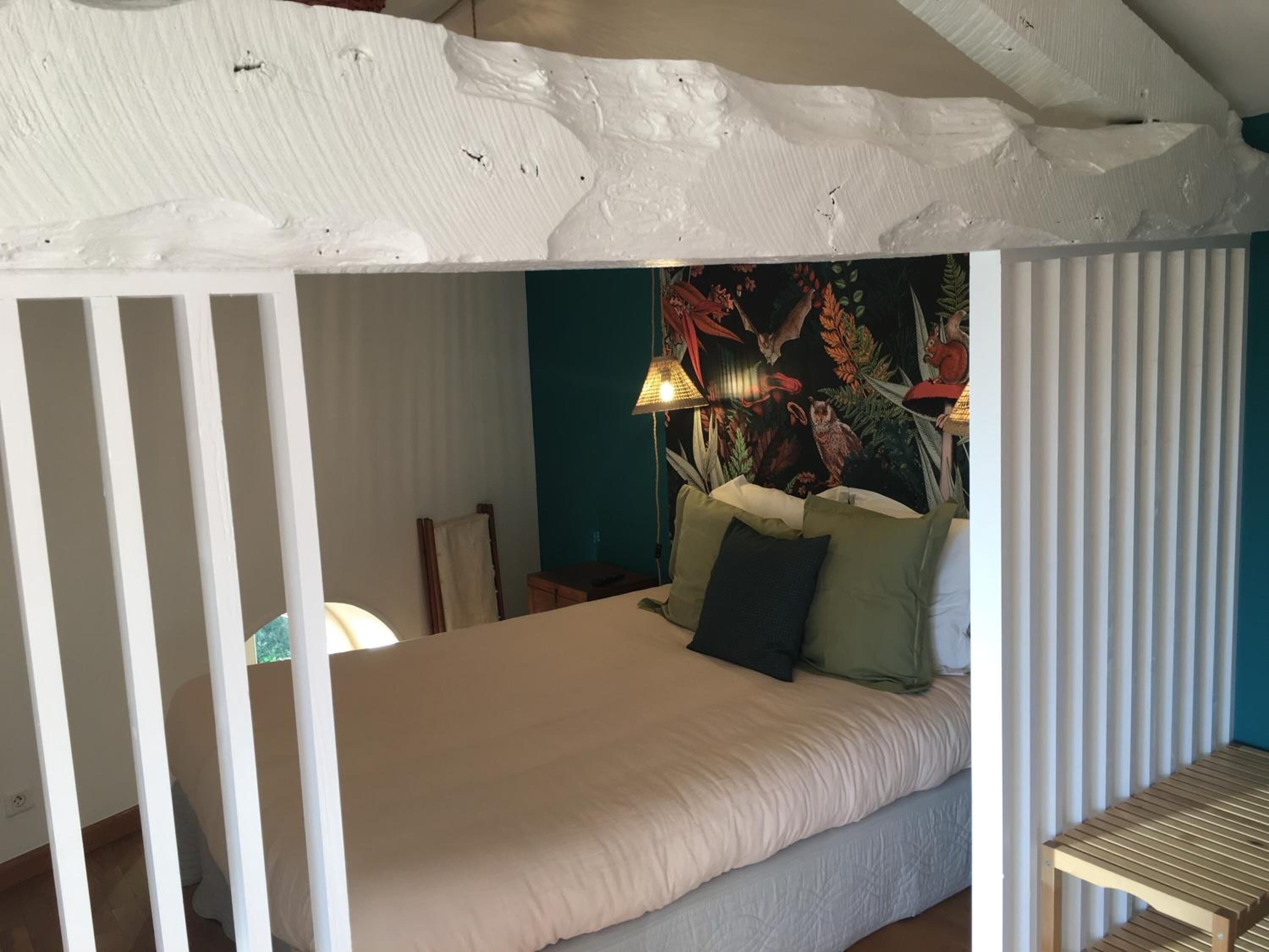 A room with a bed, a lamp, and a wall with a floral tapestry.