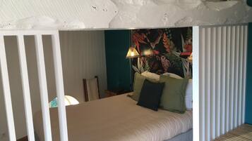 A room with a bed, a lamp, and a wall with a floral tapestry.