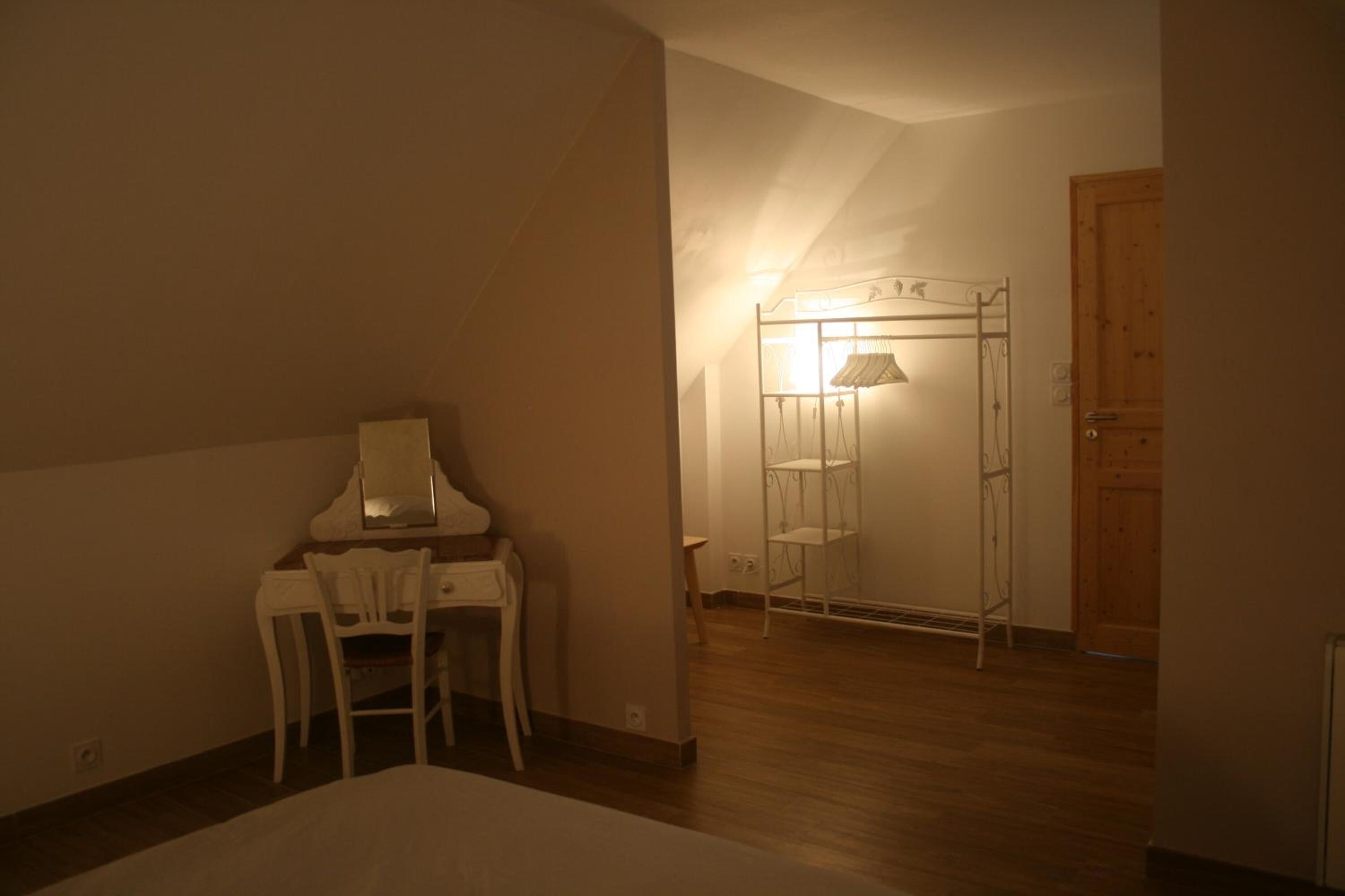 Ein Zimmer mit einem Bett, einem Schreibtisch mit Stuhl, einer Holztür und einem Metallregal mit Ablagen.