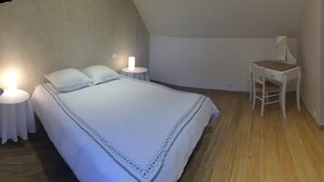 A bedroom with a large bed, two bedside tables with lamps, a wooden chair, and a small table with a tissue box.
