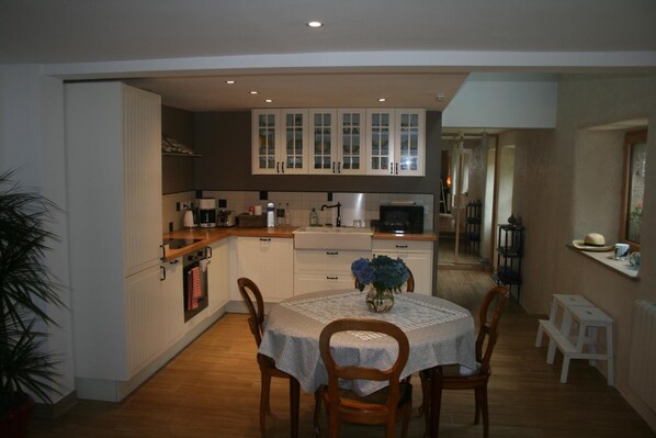 A compact kitchen with white cabinets, a dining table with chairs, and a small white stool.