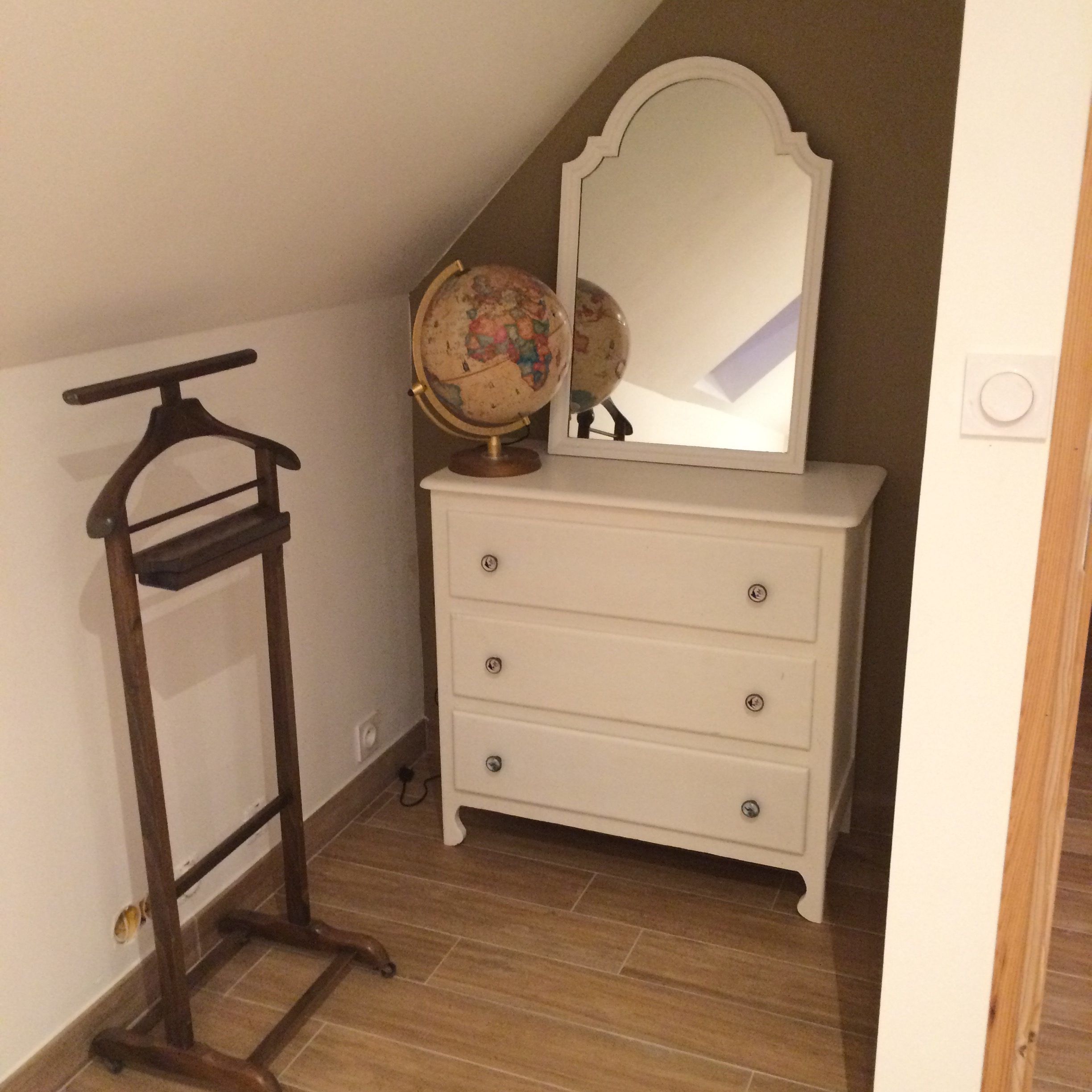 Une pièce avec une commode blanche, un cintre en bois et un globe posé sur le dessus.