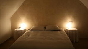 A bedroom with a sloped ceiling, two bedside tables with lamps, and a bed with pillows.