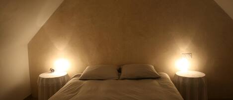 Ein Schlafzimmer mit schrägem Dach, zwei Nachttische mit Lampen und einem Bett mit Kissen.