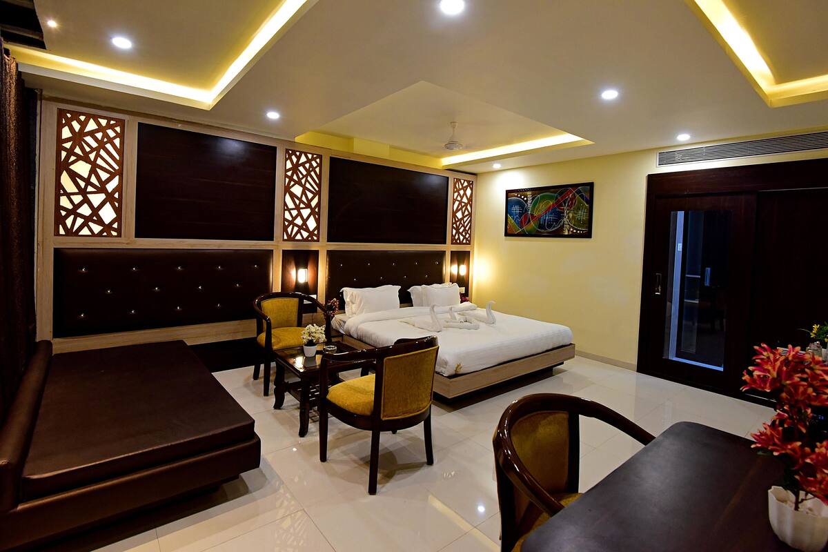 Une chambre d’hôtel moderne dotée d’un grand lit, d’un coin salon avec un canapé et des fauteuils, d’une table à manger et de panneaux muraux décoratifs.