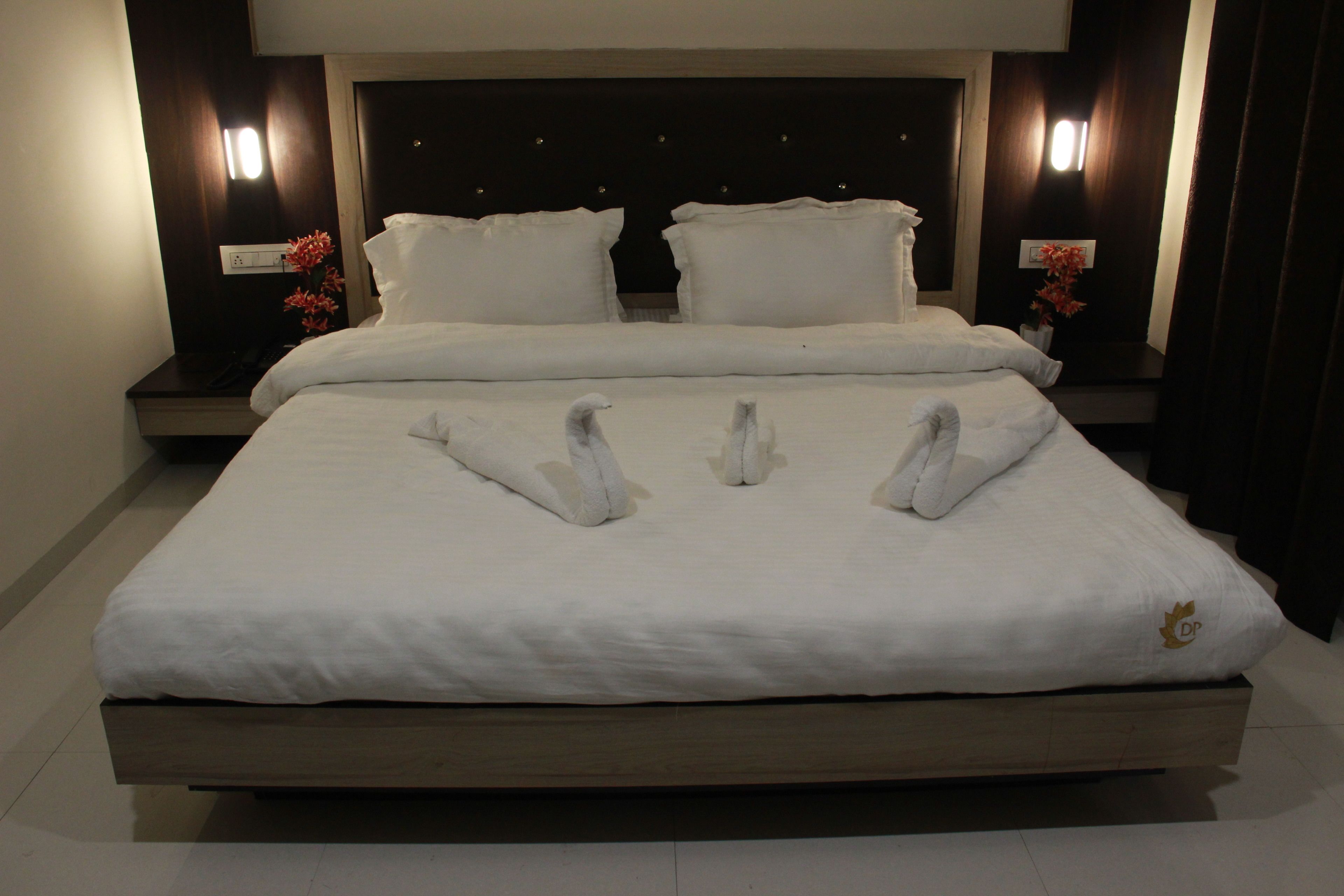 A large bed with white linens and a wooden frame, flanked by two bedside tables with lamps and a vase of flowers.