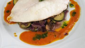 A white plate with a piece of white fish, zucchini, red onion, and a sprig of rosemary.