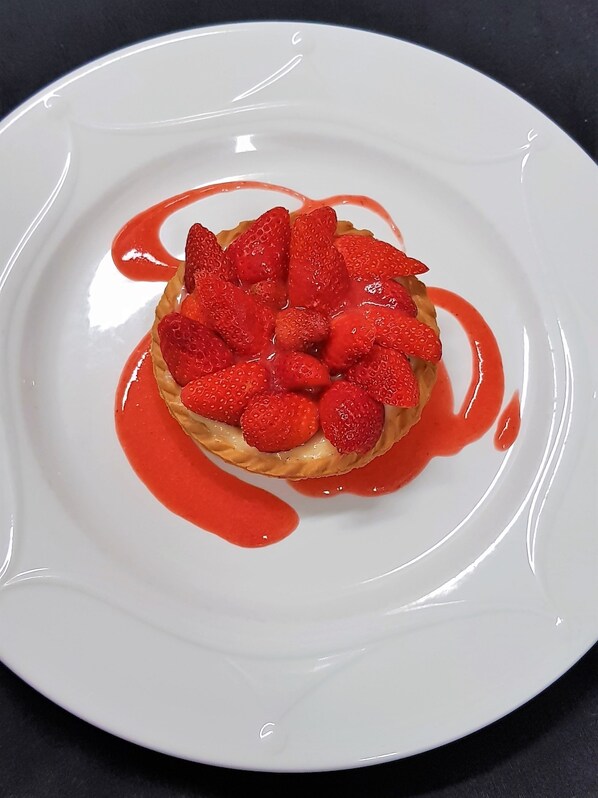 A dessert on a white plate with strawberries and red sauce. - Maison D’Hôtes Zella (Guitera-les-Baines)