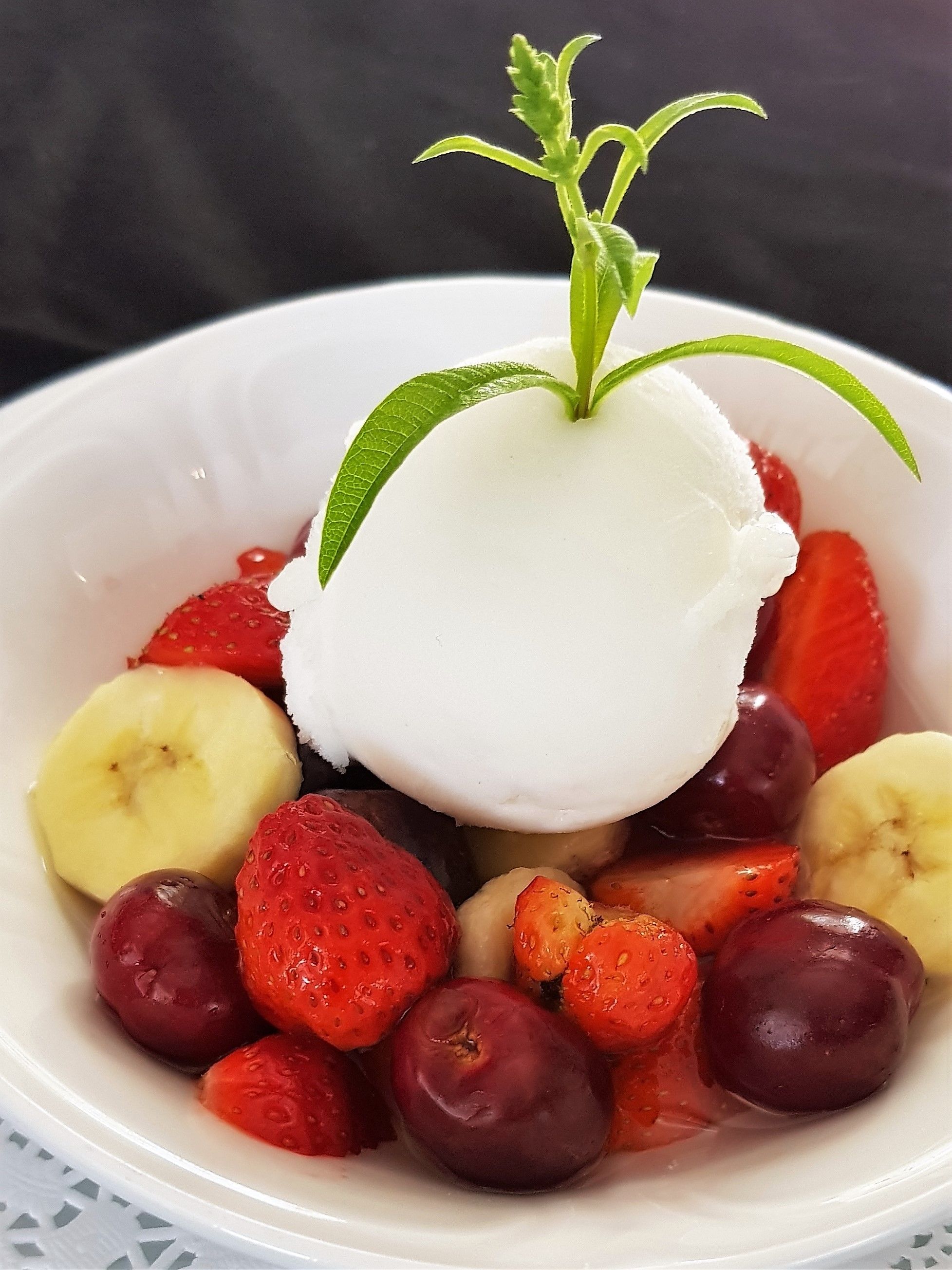 Eine Dessertschale mit Eis, Erdbeeren, Bananen und Pflaumen.