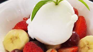 A bowl of dessert with ice cream, strawberries, bananas, and plums.