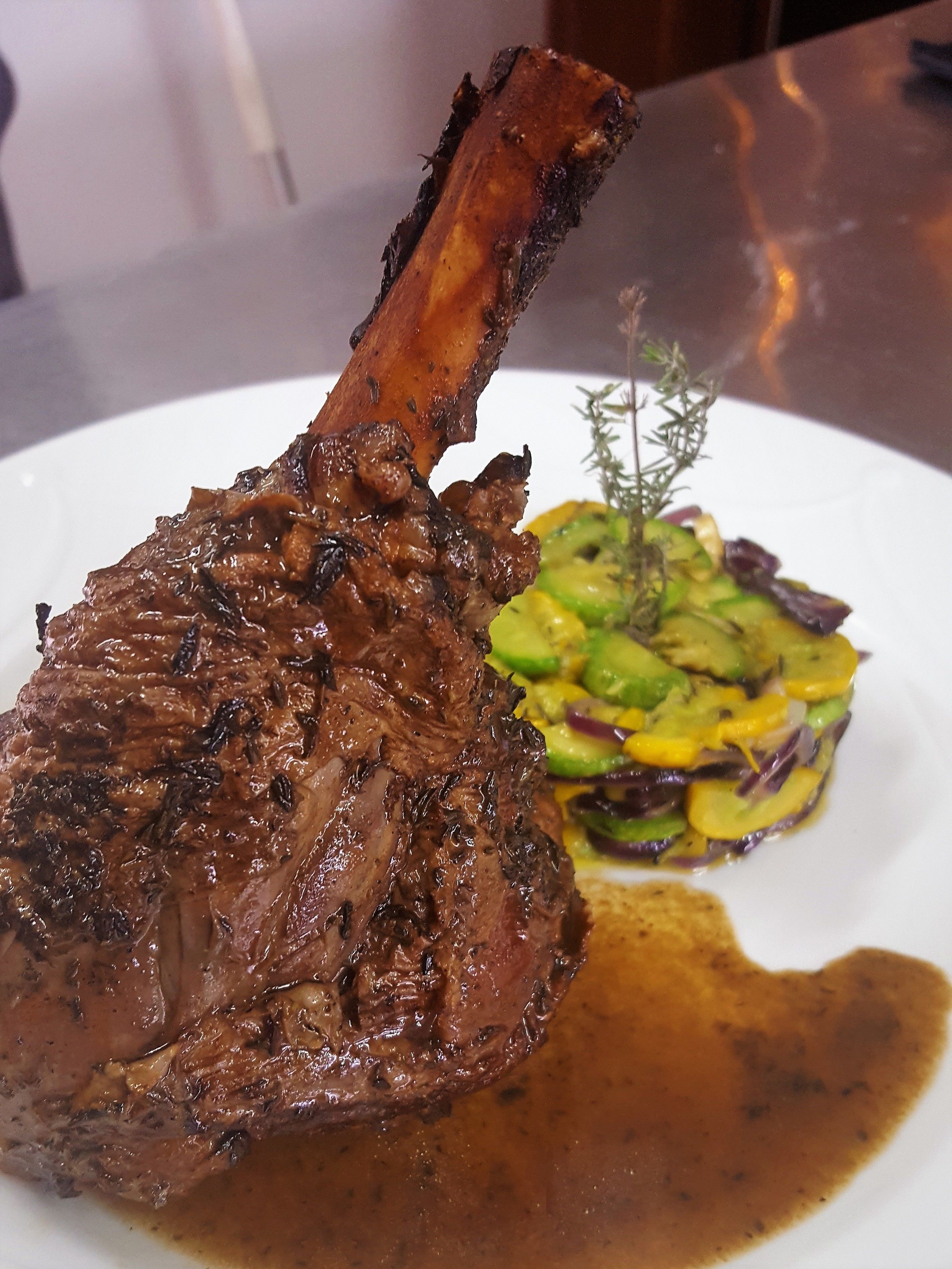 A plate with a grilled lamb shank, a side of roasted vegetables, and a sprig of thyme.