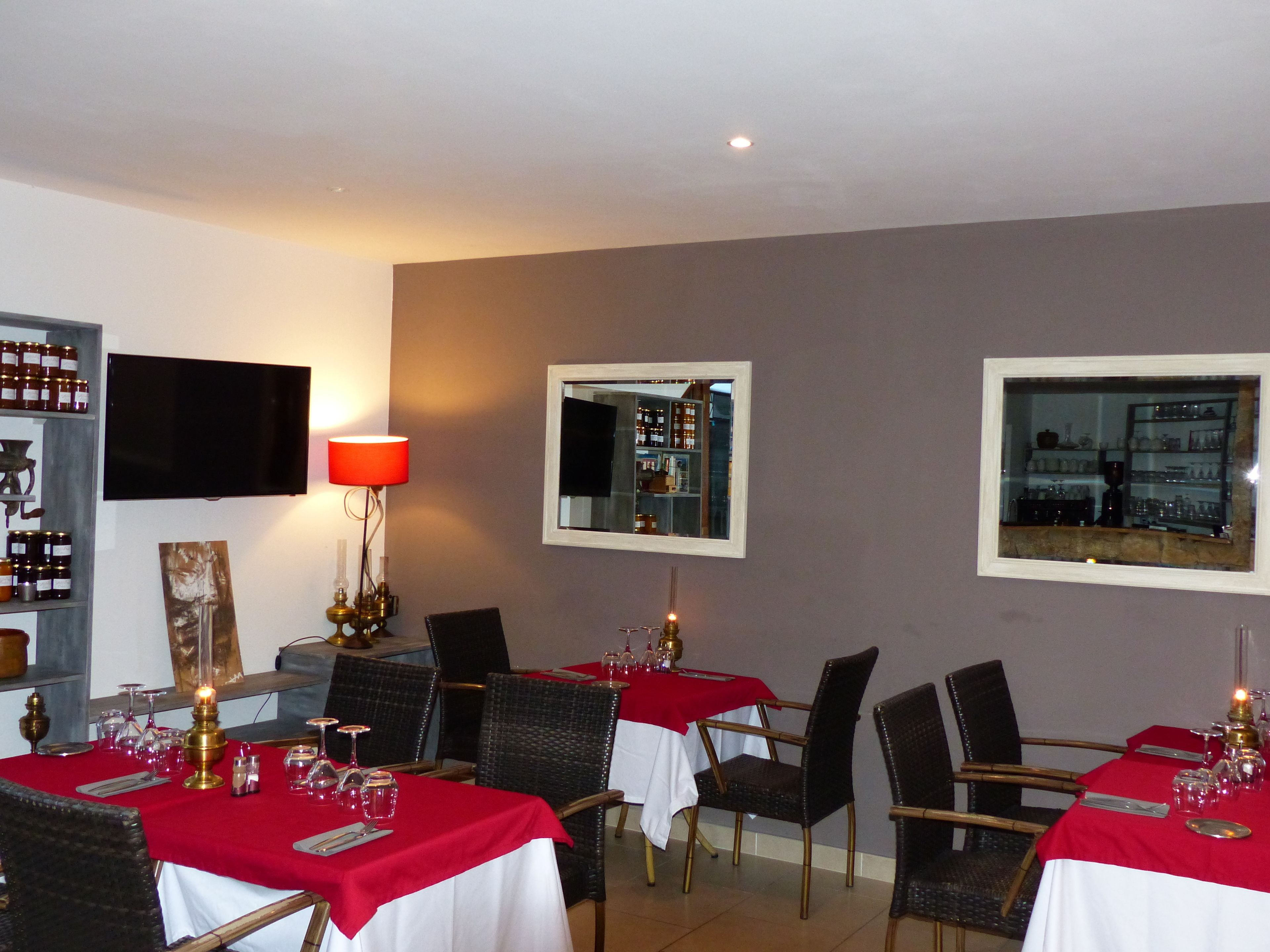 A restaurant interior with tables set for dining, a television mounted on the wall, and a wine rack.