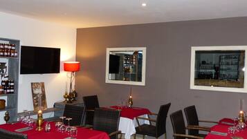 A restaurant interior with tables set for dining, a television mounted on the wall, and a wine rack.