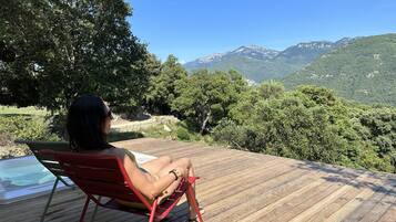 A person sitting on a red chair on a wooden deck overlooking a mountainous landscape.