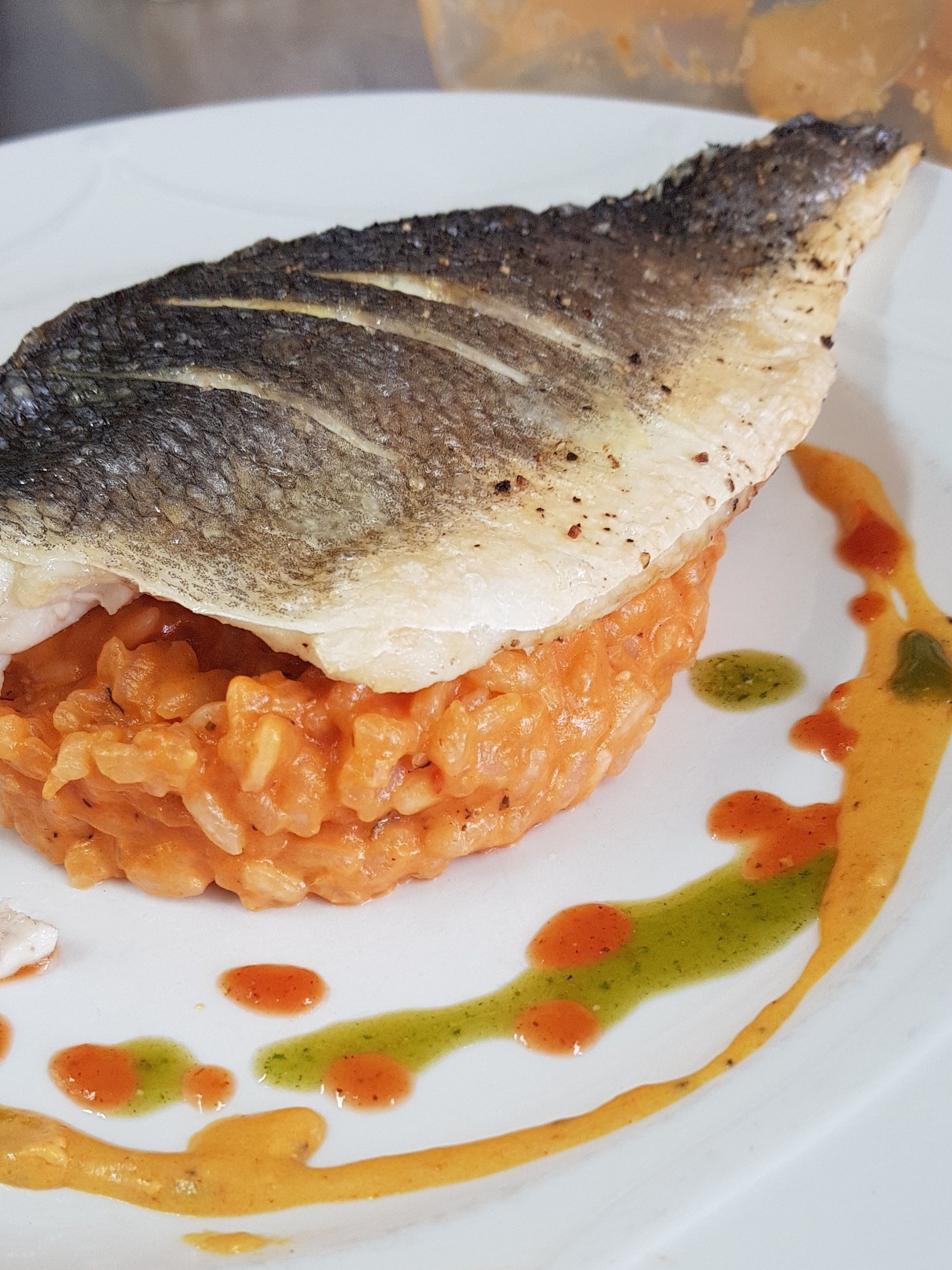A dish with a fish on top of a mound of rice, served on a white plate with colorful sauce drizzles.