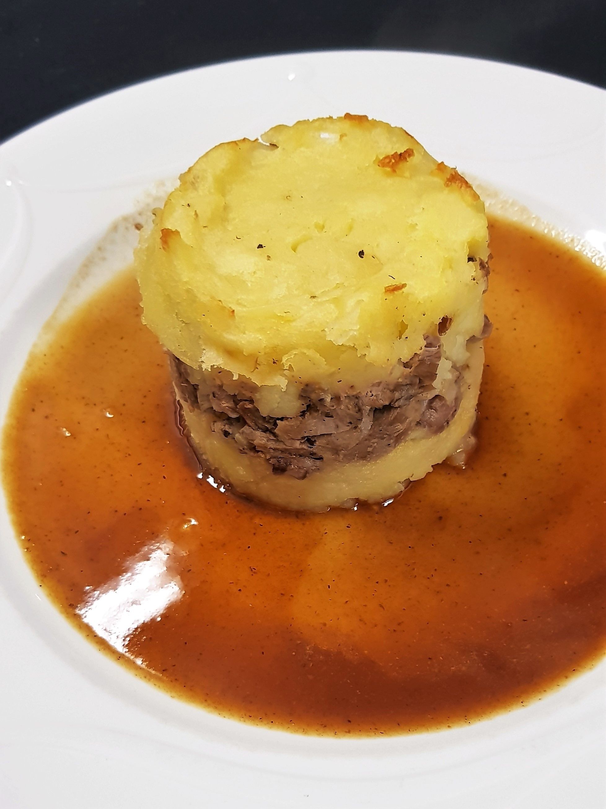 Een bord met gepureerde aardappelen en vlees, geserveerd met jus.