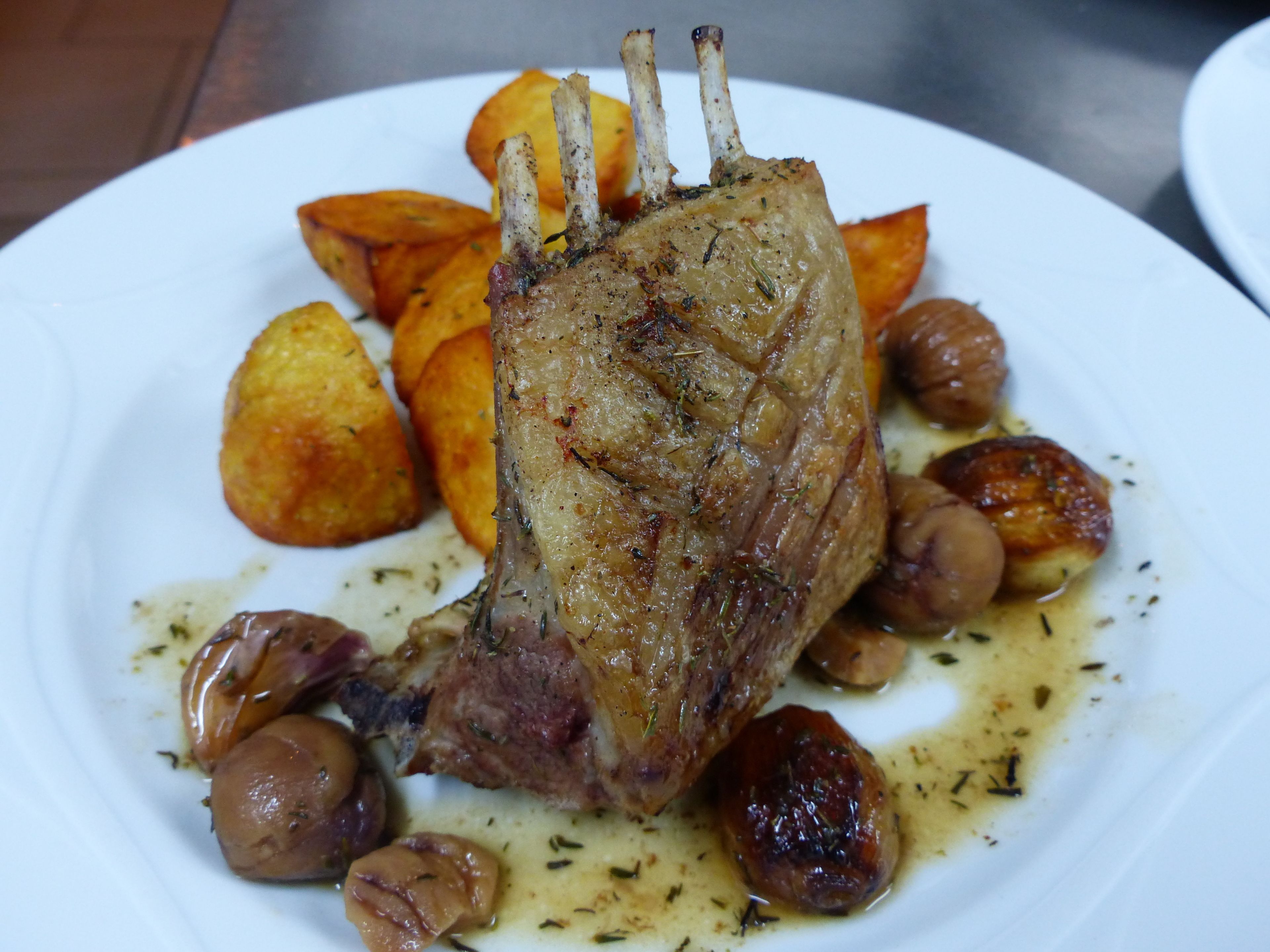 A plate with a roasted lamb shank, roasted potatoes, and roasted garlic cloves.