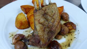 A plate with a roasted lamb shank, roasted potatoes, and roasted garlic cloves.