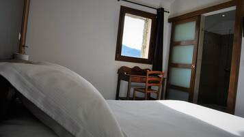 A bedroom with a bed, a desk, and a chair. There is a window with a view of the sky and a door with frosted glass panels.