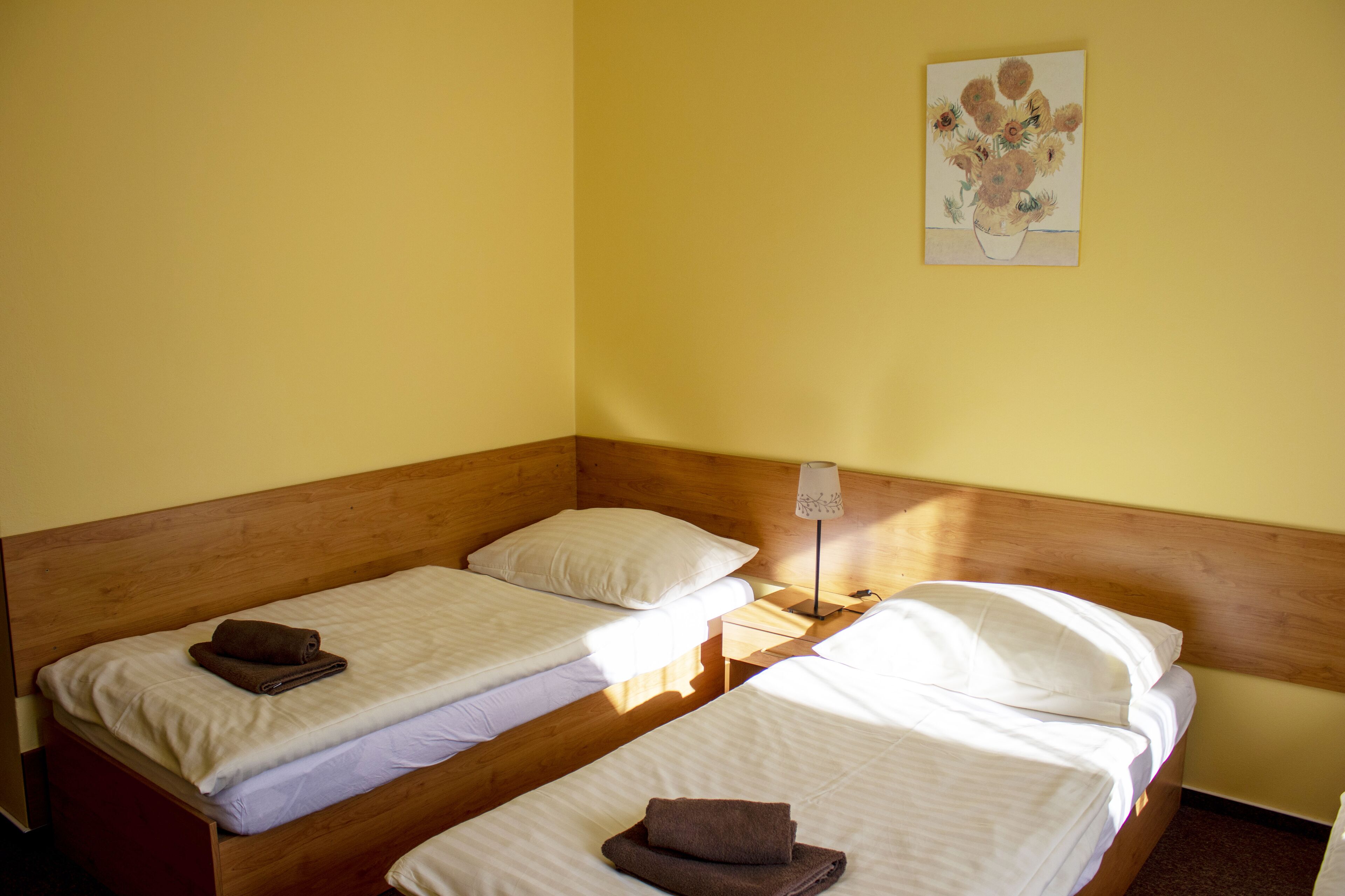A room with three single beds, wooden headboards, and a nightstand with a lamp.