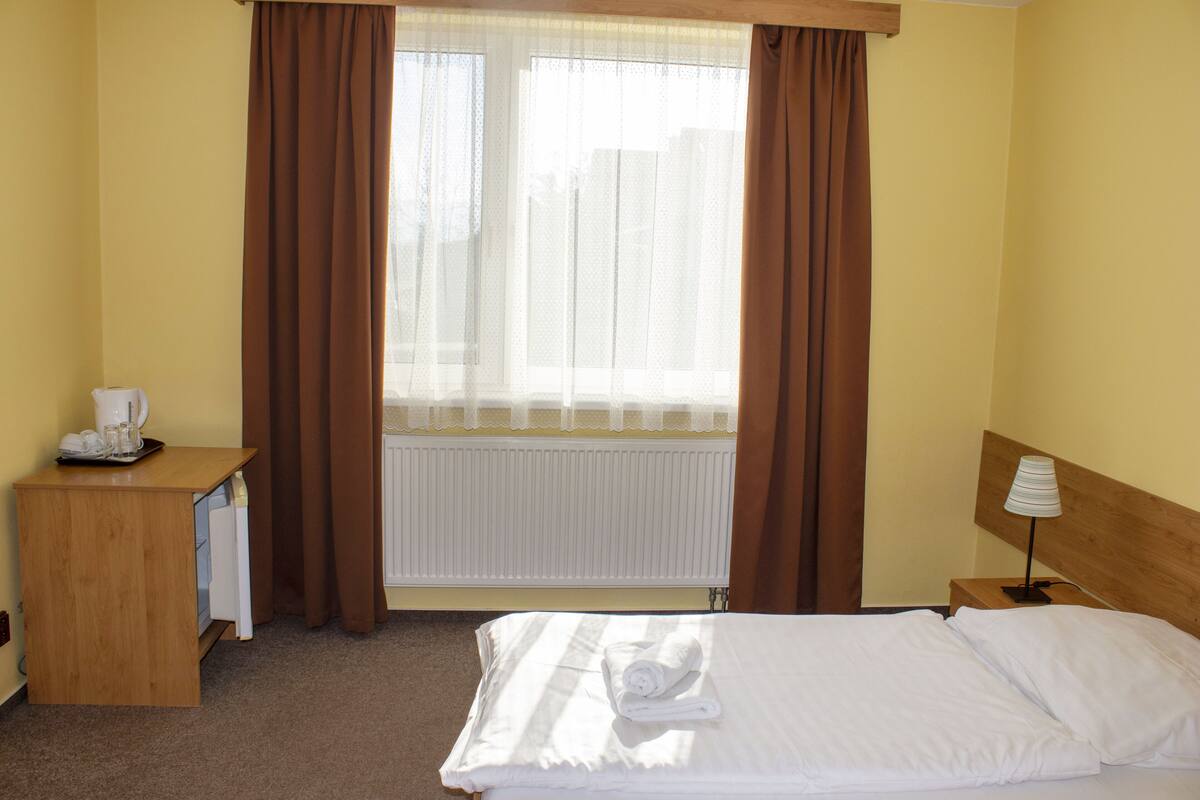 A hotel room with a bed, a desk with a telephone, a lamp, and a window with curtains.