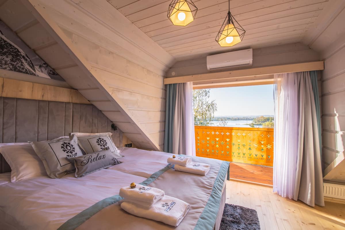 Un dormitorio con una cama grande, dos mesitas de noche, una ventana con cortinas y vistas al exterior.