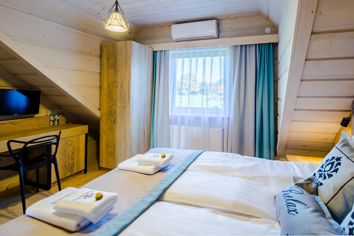 Un dormitorio con cama, escritorio con televisor y ventana con cortinas.