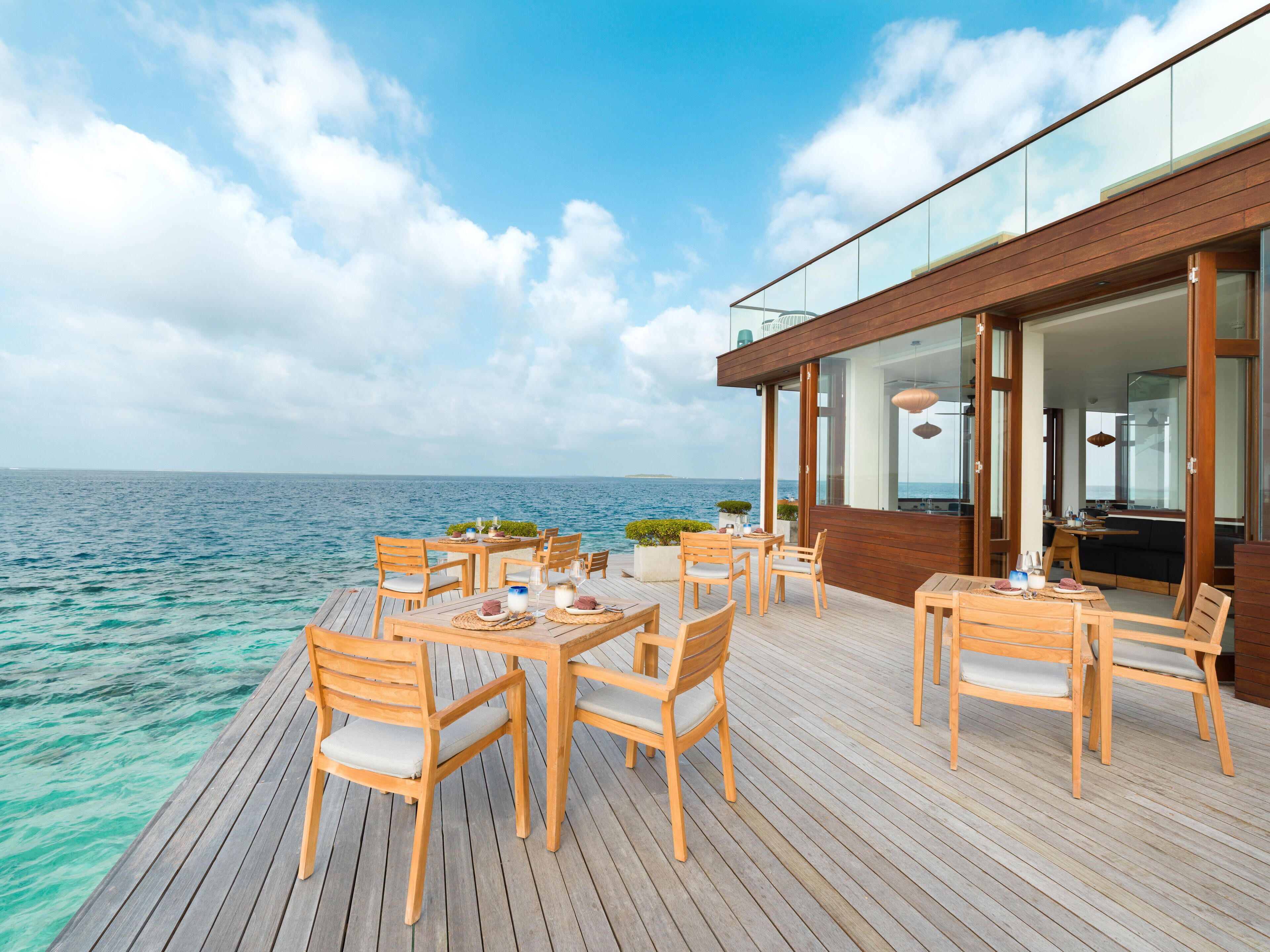 Una terraza de madera con mesas y sillas que da al mar.