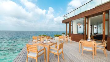 Una terraza de madera con mesas y sillas que da al mar.