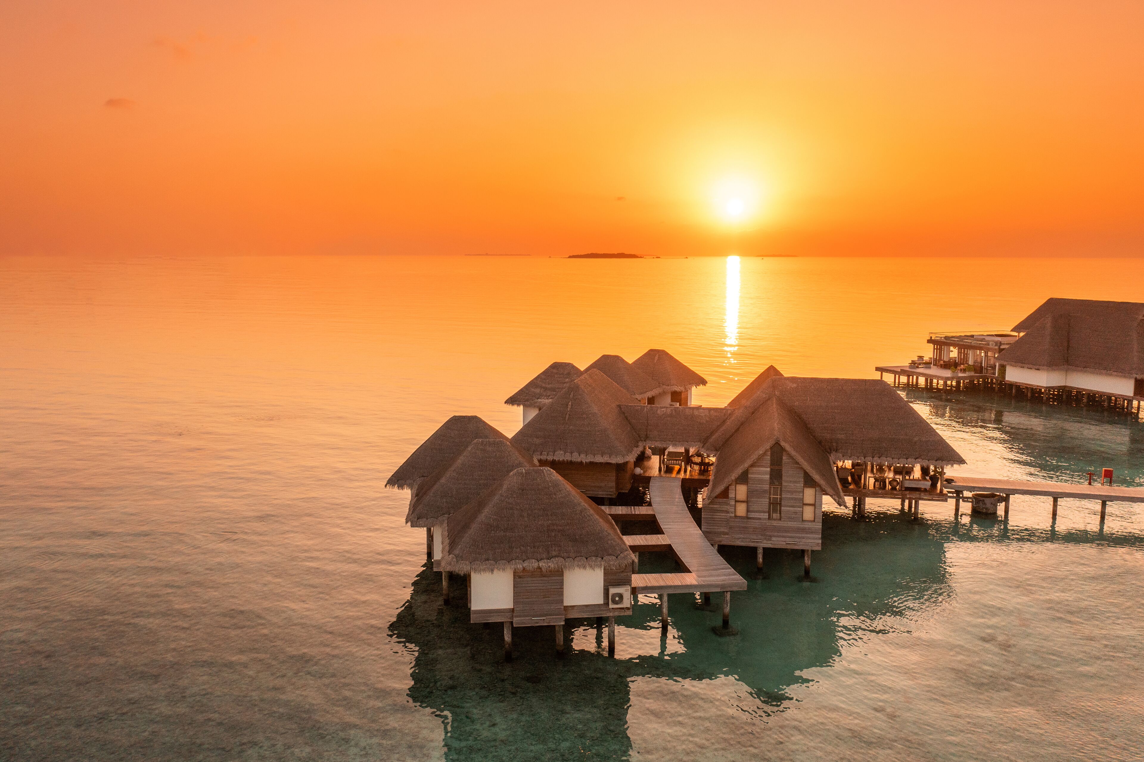 Wasserbungalows mit Strohdächern, verbunden durch Wege über klares türkisblaues Wasser.